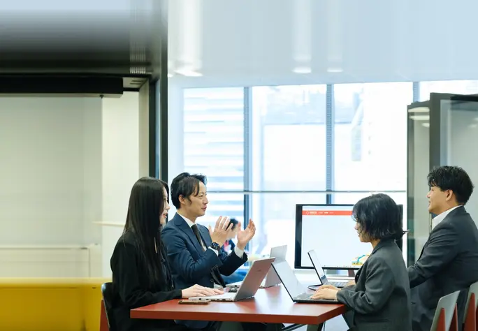 ノートパソコンを広げてテーブルを囲み話し合う社員