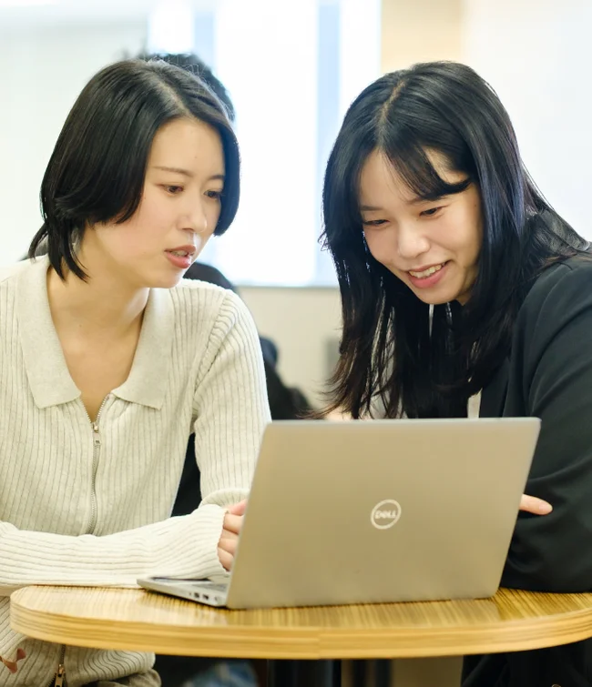 ノートパソコンをのぞき込みながら話す二人の社員