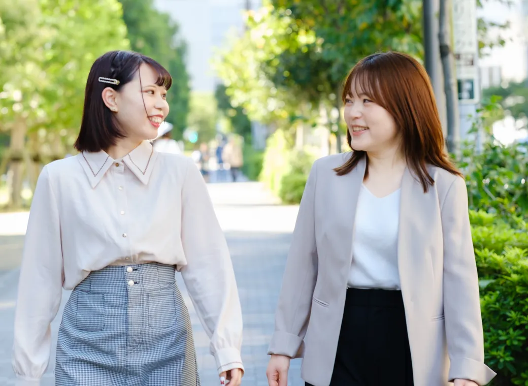 並木道を並んで歩きながら笑顔で話す社員2人