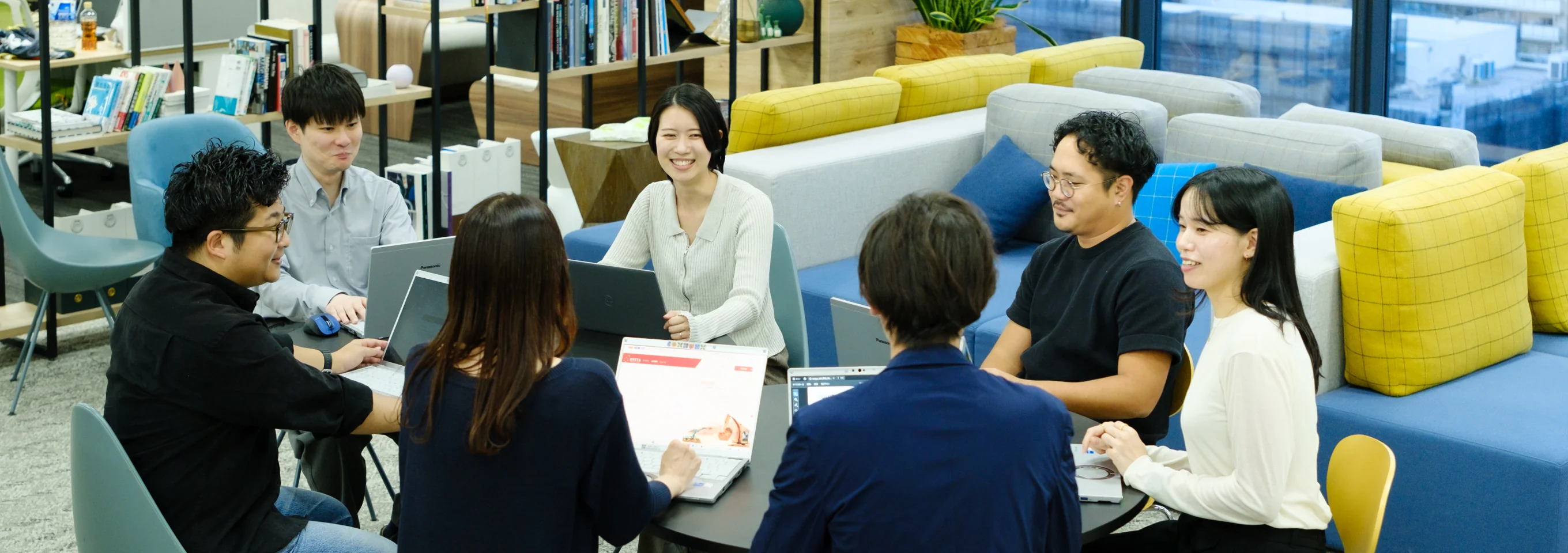 ソファ席でノートパソコンを囲んで話す社員たち