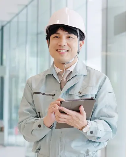 ヘルメットをかぶりタブレットを持つ作業着姿の男性
