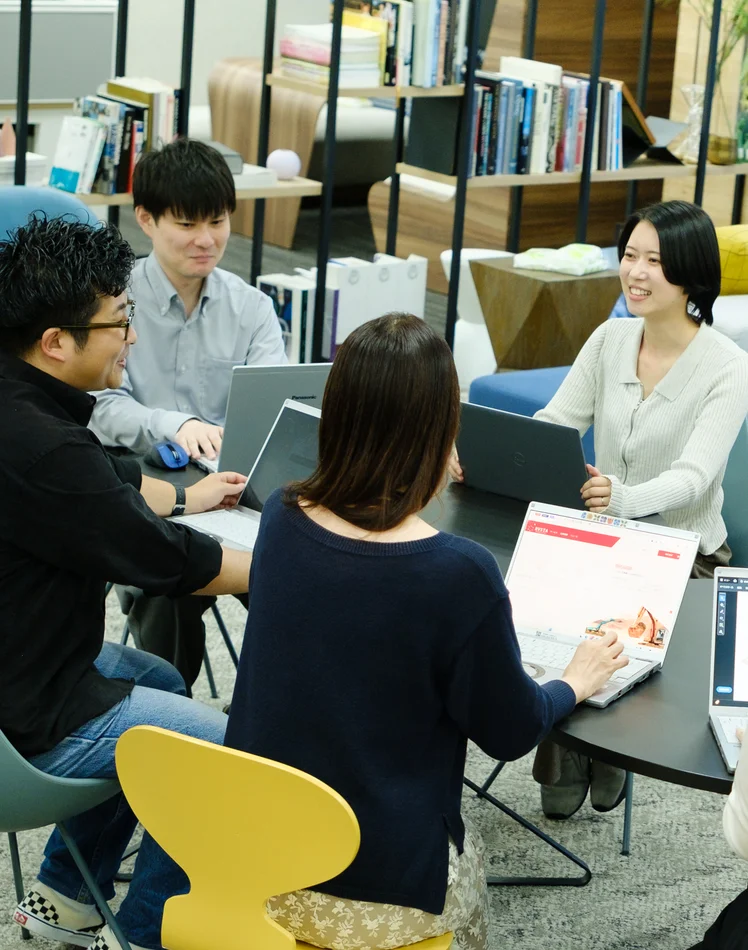 ラウンジでノートパソコンを囲んで打ち合わせをする社員たち