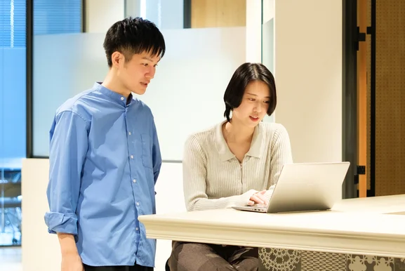 ノートパソコンに向かう社員と、横から画面をのぞき込む社員