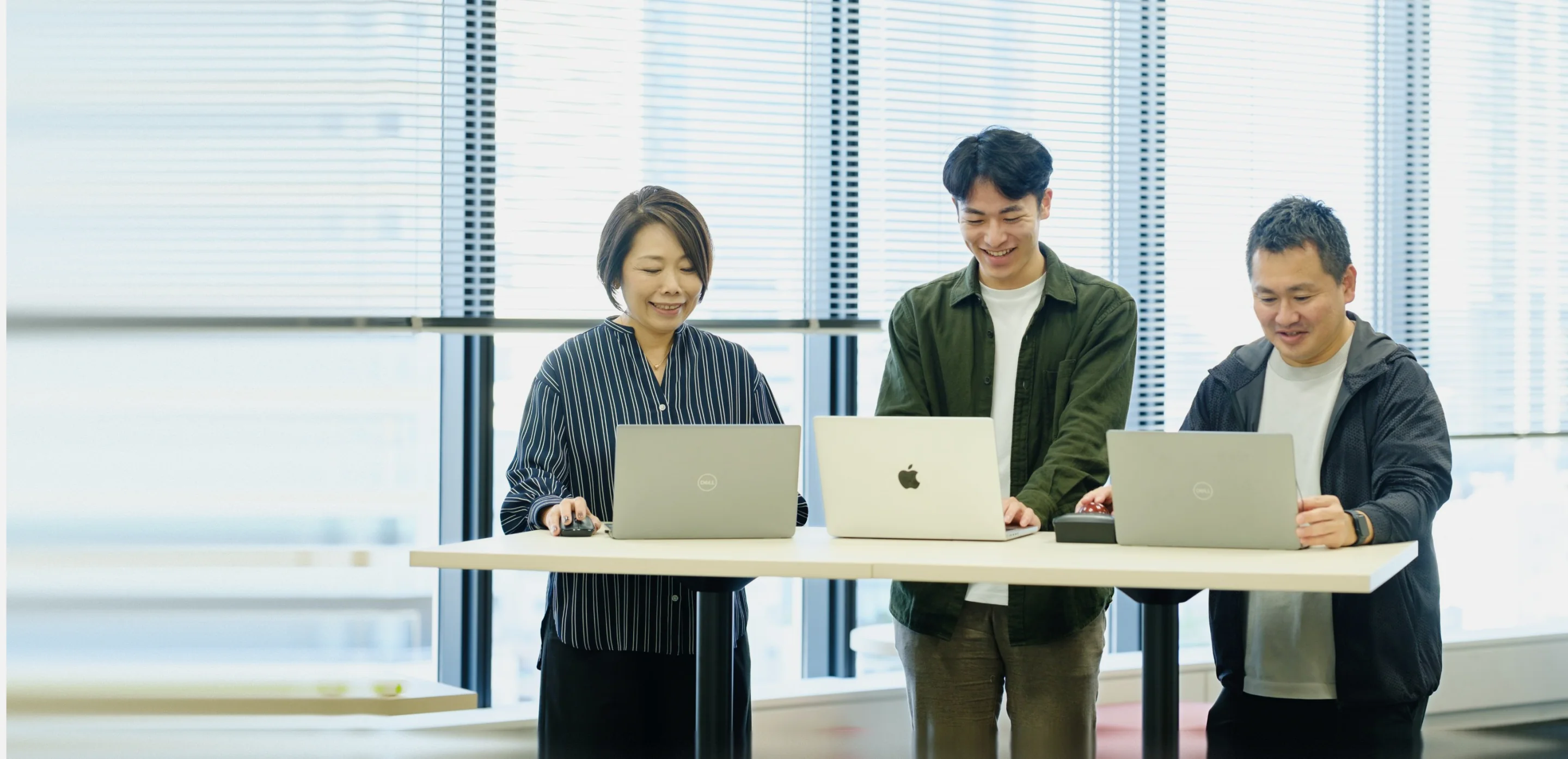 ノートパソコンを囲んで立って話す3人の社員