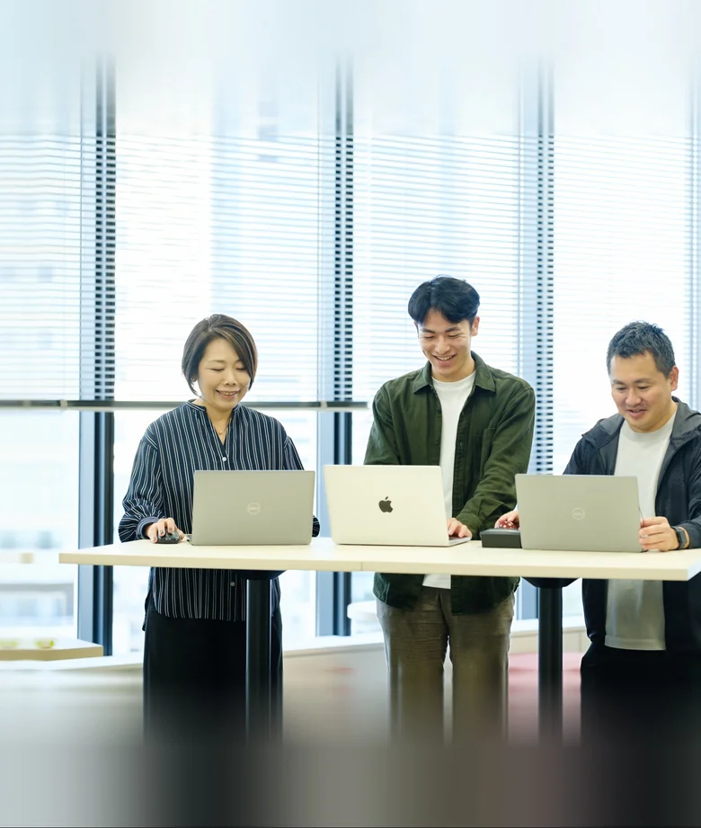 ノートパソコンを囲んで立って話す3人の社員
