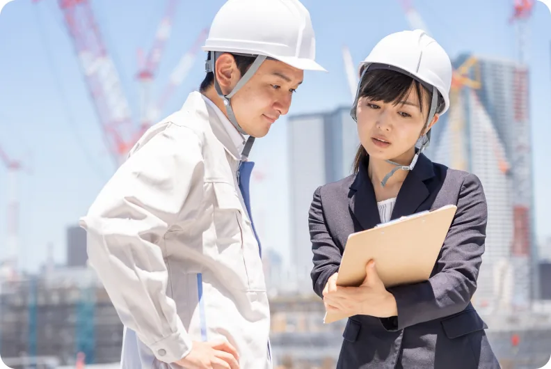 建設現場でヘルメットをかぶって打ち合わせをする二人