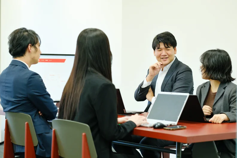 ノートパソコンを広げたテーブルで話し合う社員たち
