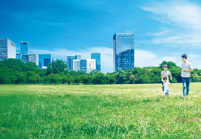 高層ビルを背に芝生の広場を駆ける親子
