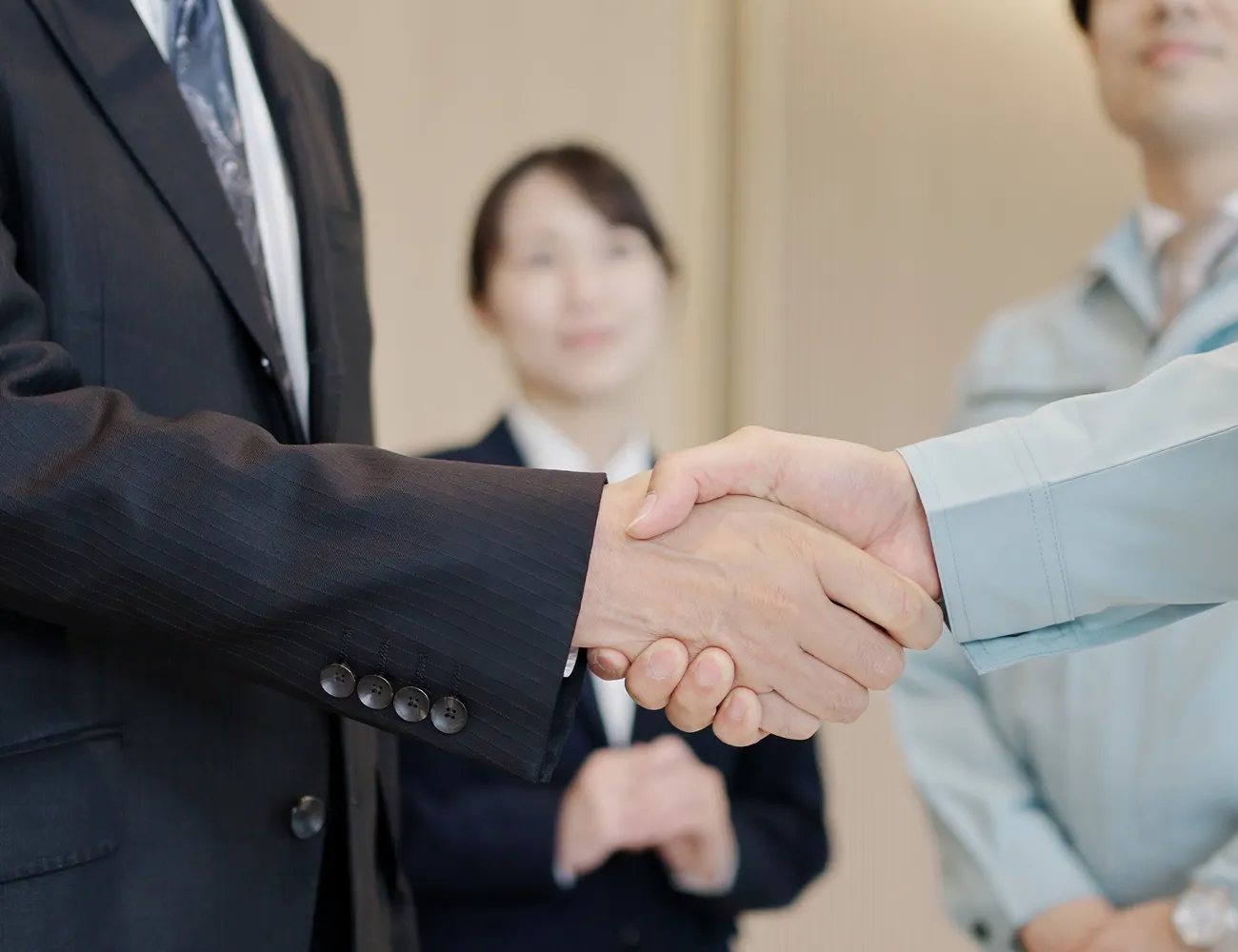 スーツ姿の社員と作業服姿の技術者が握手する様子
