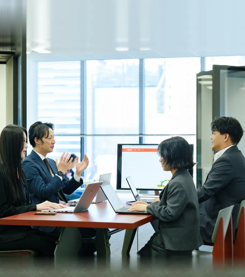 ノートパソコンを広げてテーブルを囲み話し合う社員