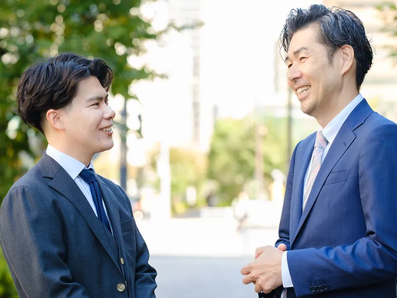 屋外で笑顔で話すスーツ姿の社員