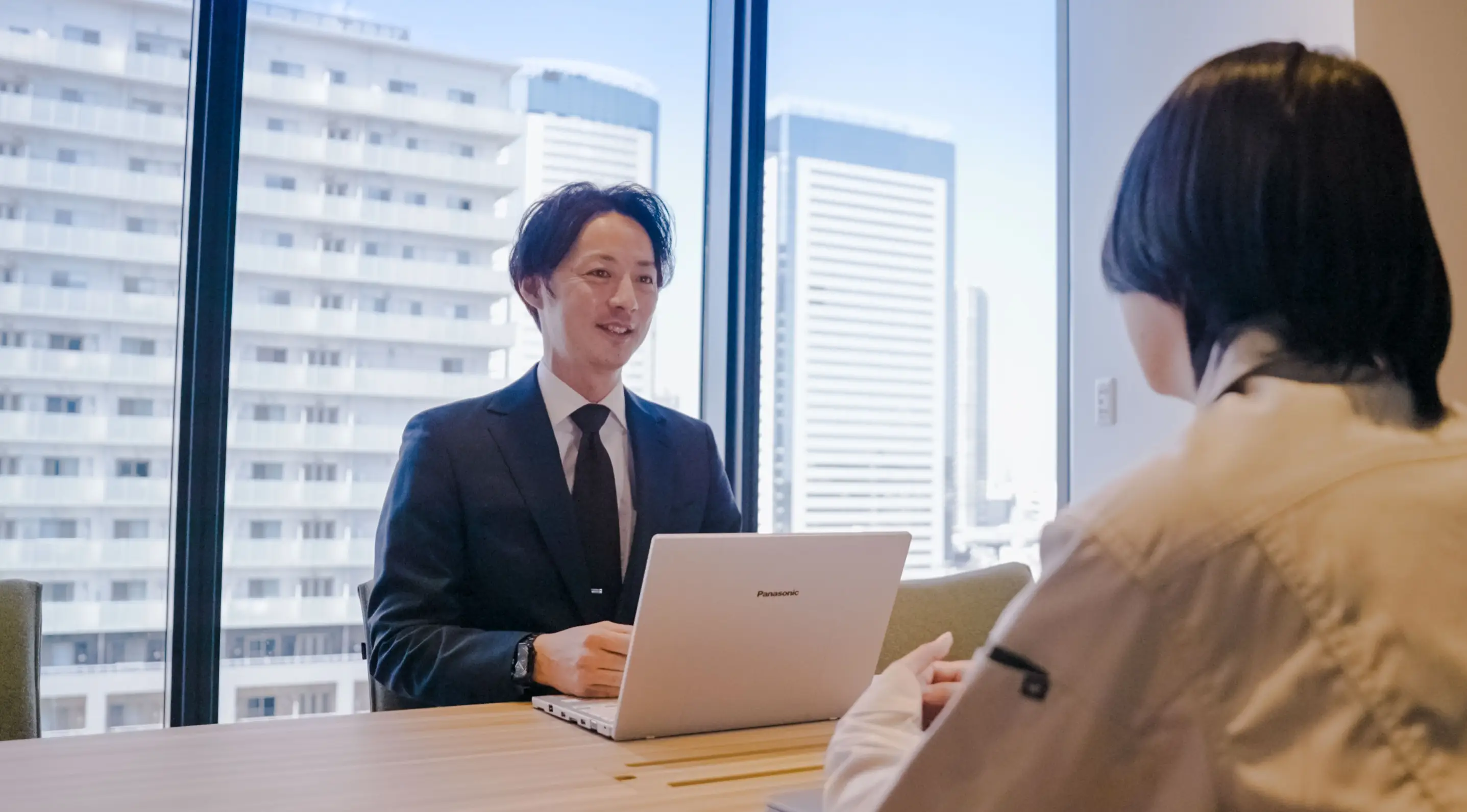 ノートパソコンを前に話すスーツ姿の社員